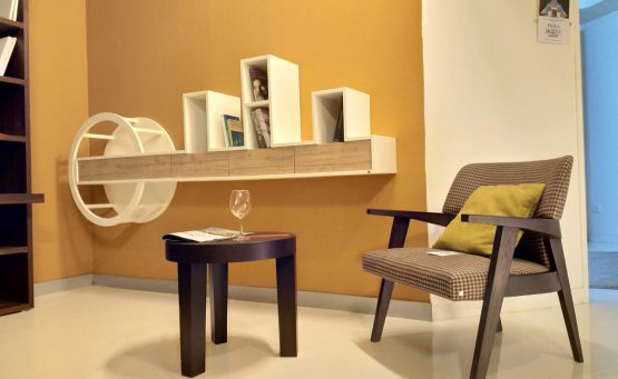 Room furnished with a wooden armchair, a three-legged table and a wooden wall shelf