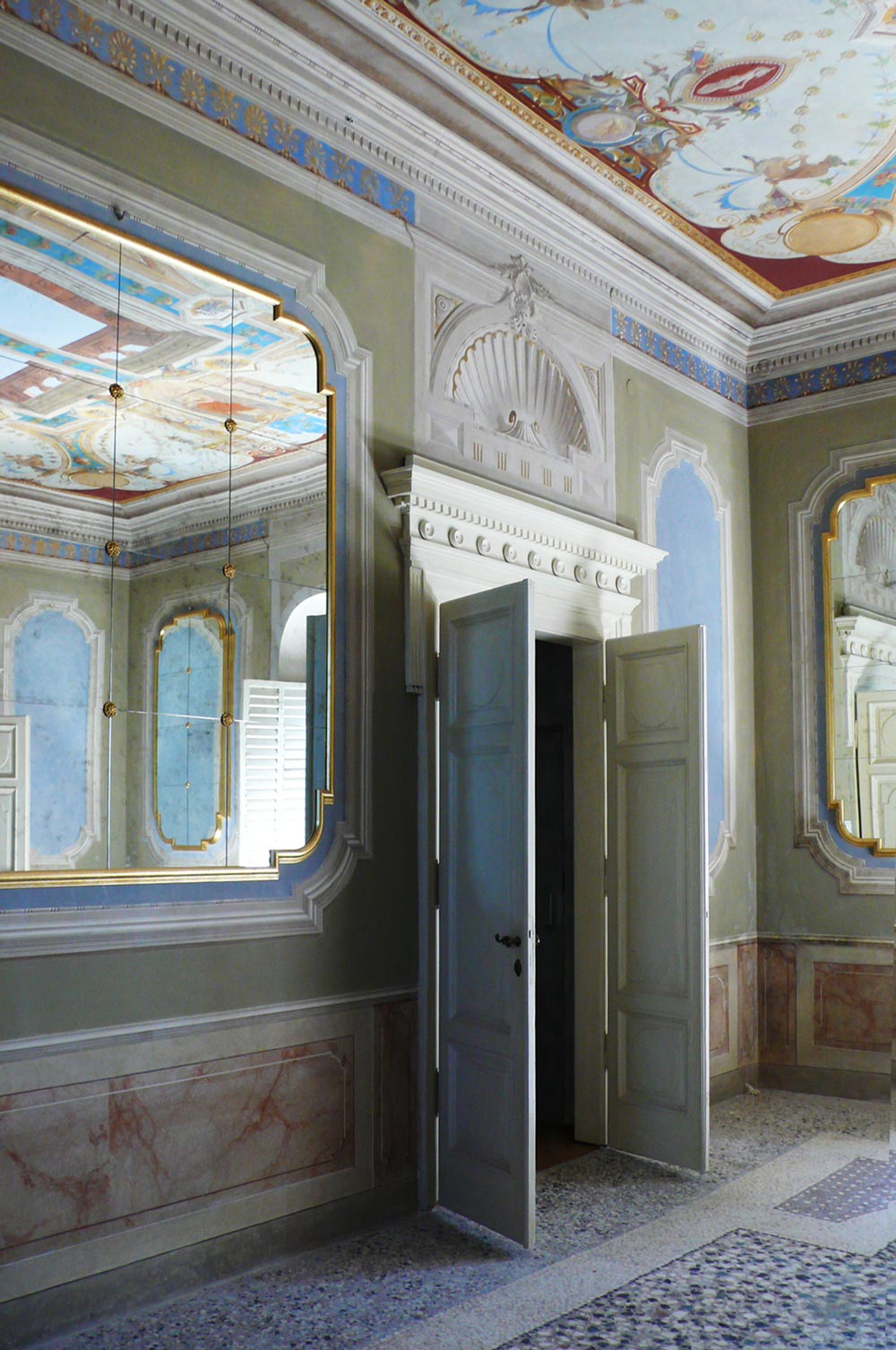 Stanza decorata di una villa con una porta bianca e a fianco uno specchio a muro