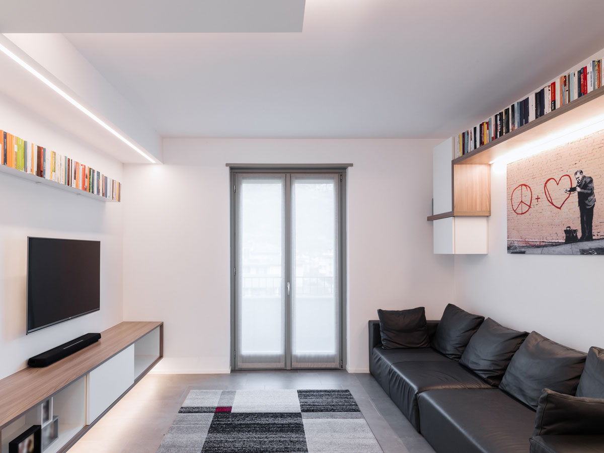 Living room with a black leather sofa on the right, a television on the left above a wooden cabinet and a central door