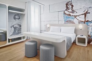 White double bed in a room with some figures painted on the wall and in the wardrobe