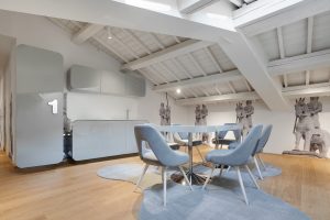 Open space with wooden floor and ceiling and gray table and kitchen