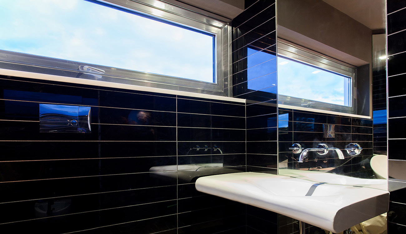 Washbasin alongside a wall with black tiles and a small window