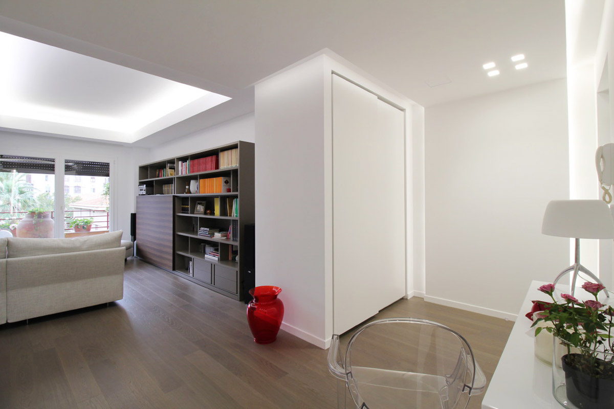 Living room with sofa and wall bookcase that leads to the entrance