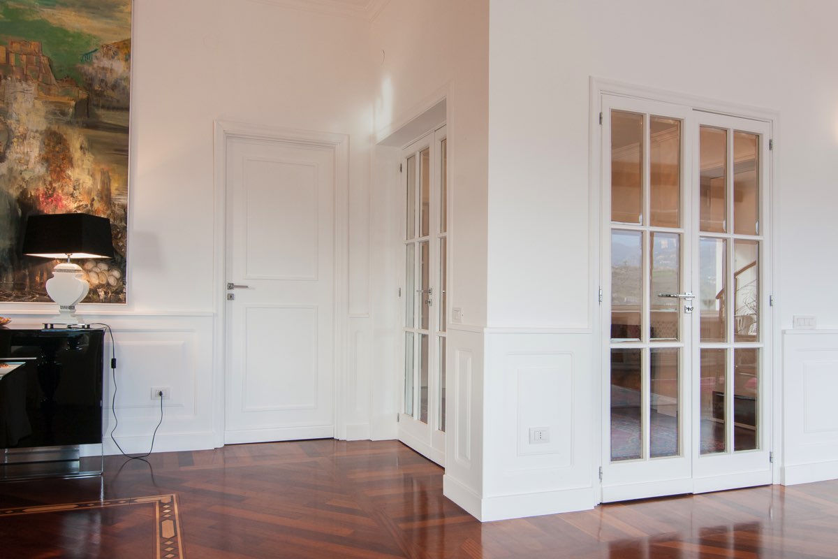 nel salone la boiserie bianca corre sulle pareti, spezzata dalle porte
