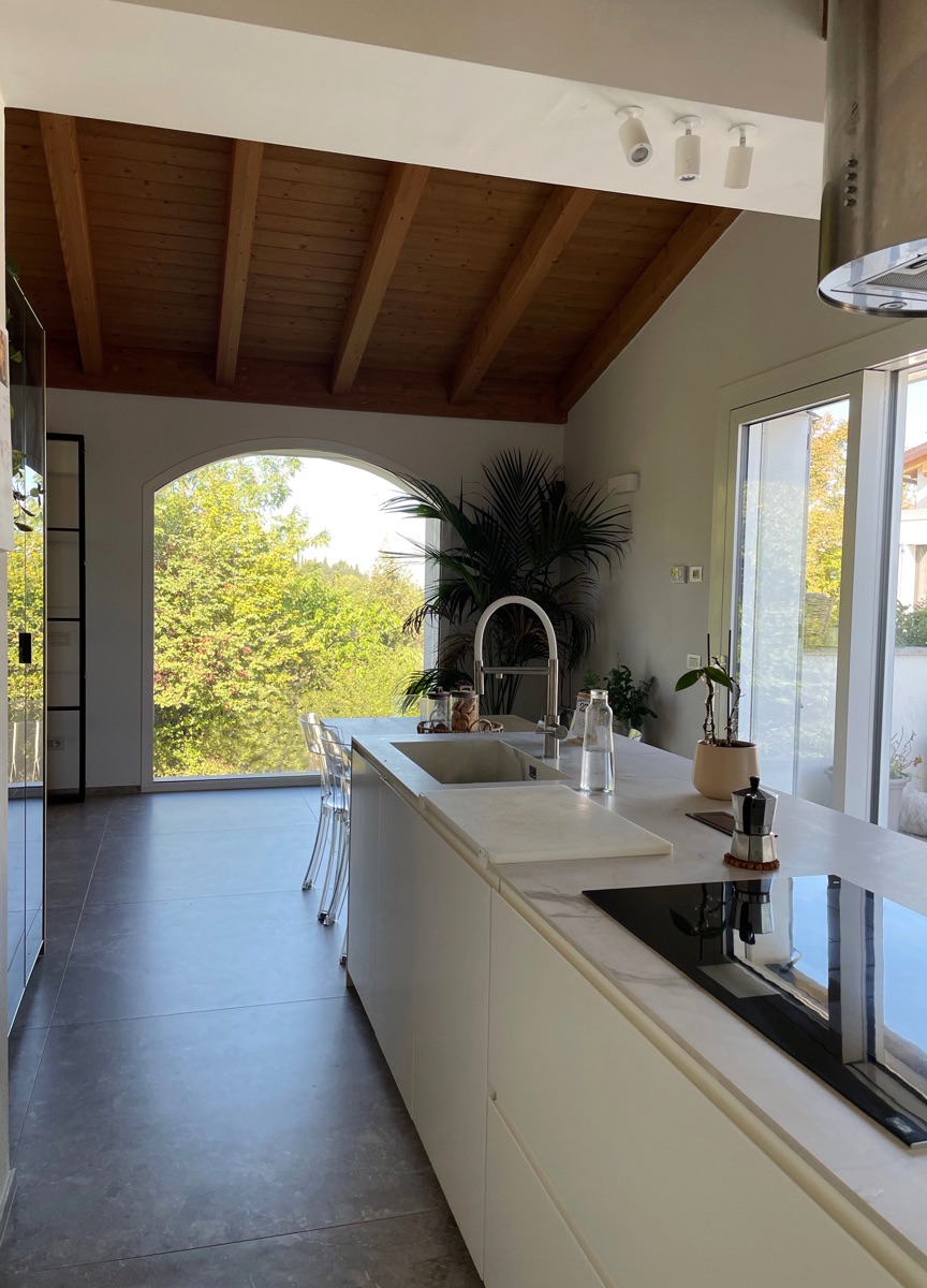 Modern kitchen in the TR House with marble island, built-in table and arched window framing the outside view, by twoPIU architects