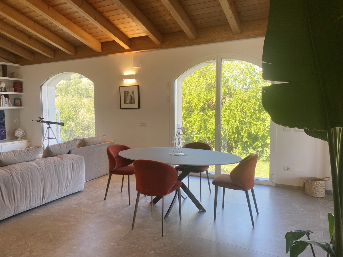 Open living space in TR House with large dining table, red chairs and exposed wooden beams, designed by twoPIU architects