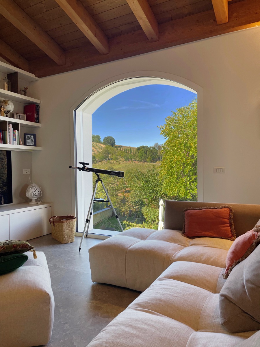 Cozy lounge area in the TR House with soft sofa and large arched window offering views of the green outside, created by twoPIU architects