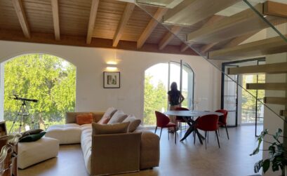 Zona pranzo della TR House adiacente a una scala moderna con balaustre in vetro e vista sul soggiorno a doppia altezza, creata da duePIU architects