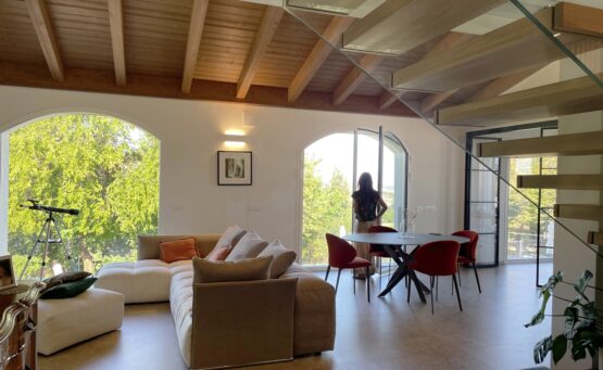 Zona pranzo della TR House adiacente a una scala moderna con balaustre in vetro e vista sul soggiorno a doppia altezza, creata da duePIU architects
