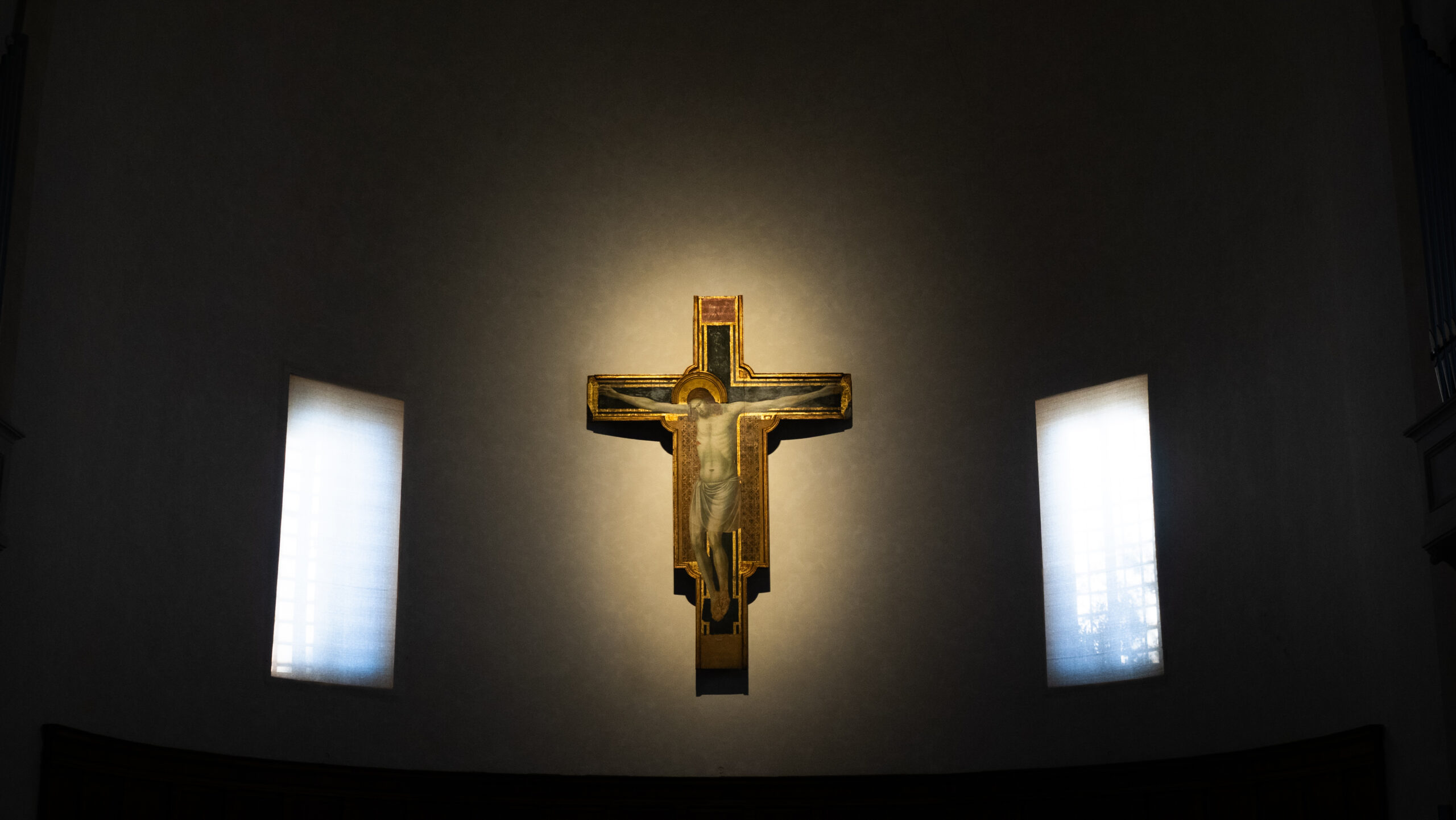 Un crocifisso semplice ma di grande effetto, illuminato su una parete semplice sopra l'altare centrale di una chiesa.