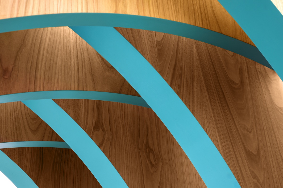 Dettaglio di una struttura in legno con elementi arcuati dipinti di blu, che creano un design dinamico e moderno. La combinazione del legno naturale con i dettagli colorati crea un effetto visivo interessante.