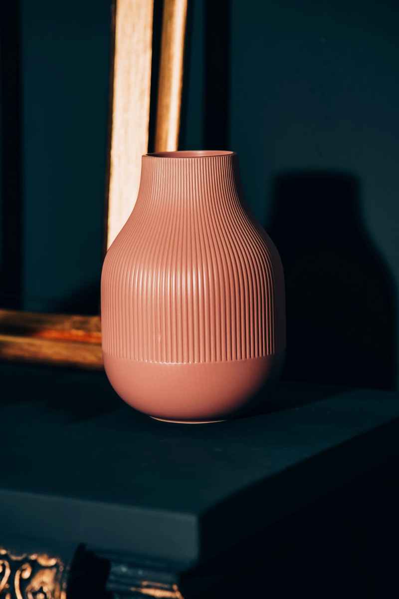 Vaso decorativo rosa dal design minimalista, posizionato su una superficie scura con sfondo in ombra